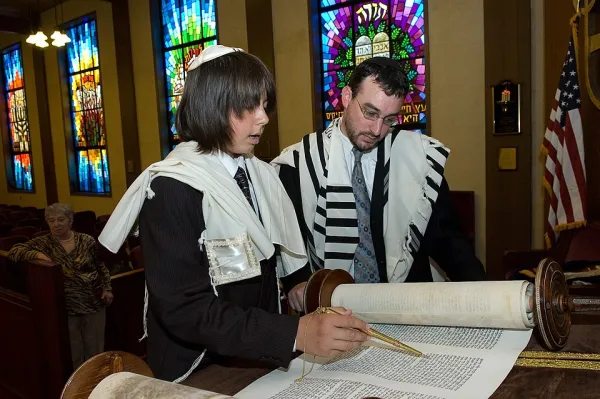 A young person wearing a tallit and tefillin for the first time at their bar mitzvah