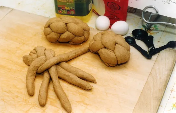 Hands braiding challah dough into the traditional loaf shape