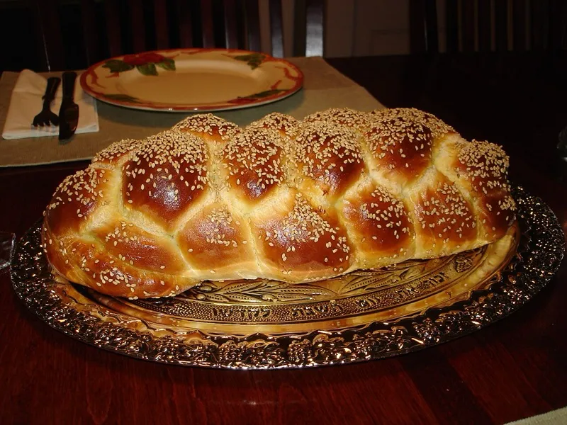An assortment of Jewish breads including challah, bagels, and pita arranged on a wooden table