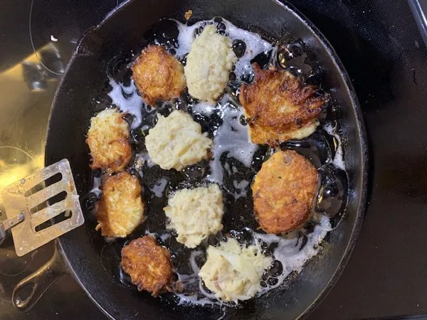 Potato latkes frying in a hot skillet with oil
