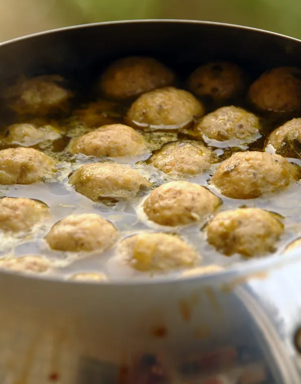A traditional bowl of matzo ball soup being prepared with golden chicken broth