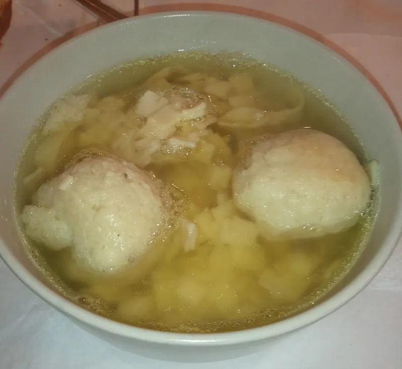 A bowl of golden matzo ball soup with fluffy matzo balls and fresh dill