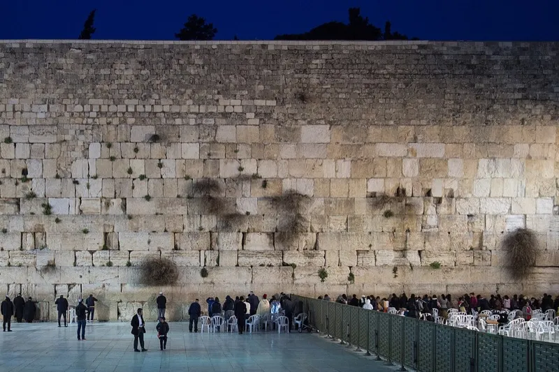 The Western Wall (Kotel) in Jerusalem illuminated at night with worshippers in the prayer plaza